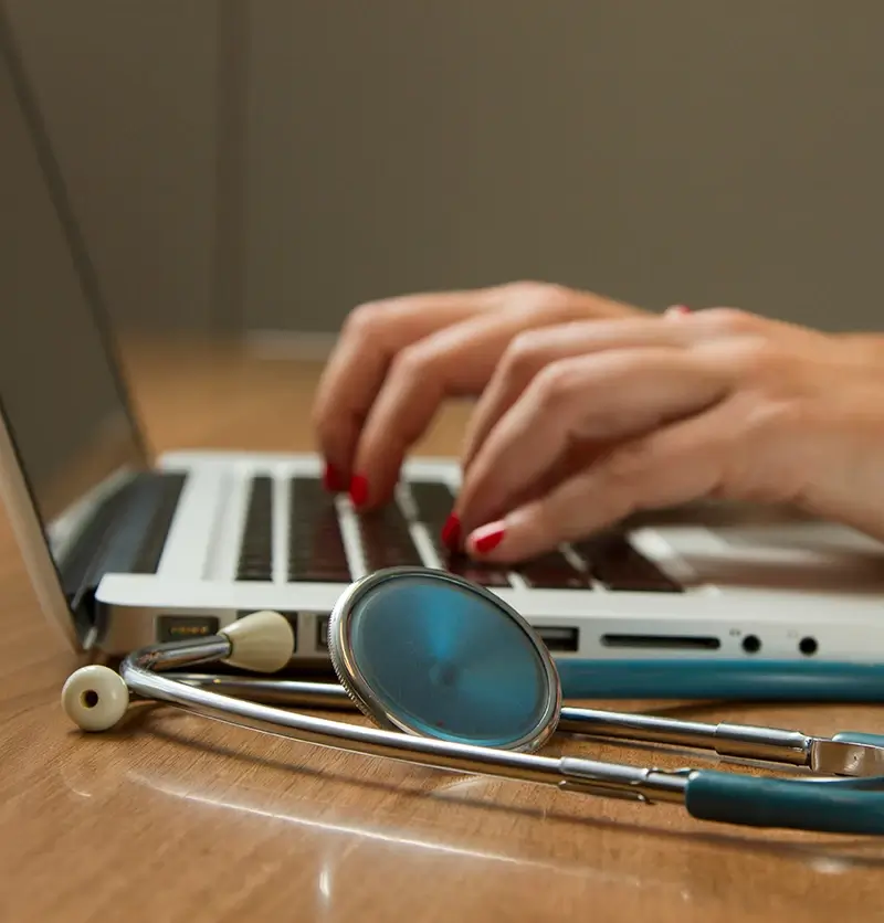 Person typing on computer next to stethoscope